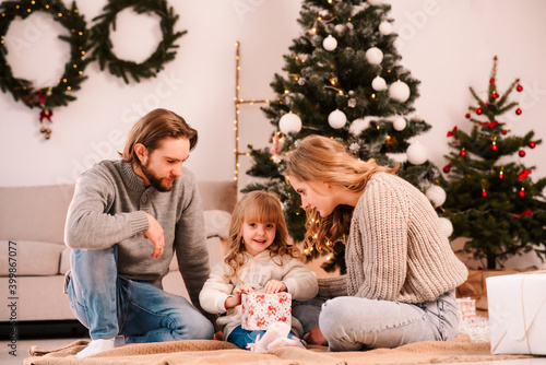 Parents give Christmas gifts box to their daughter while sitting in the room on the floor