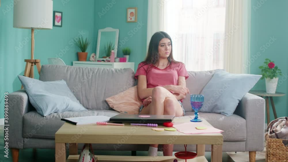 Young pretty woman in casual outfit is sitting on sofa at home, feeling sad and offended, has rather boring time indoor, negative mood, Slow motion. Young pretty woman in casual outfit is sitting on sofa at home, feeling sad and offended, has rather boring time indoor, negative mood, Slow motion.