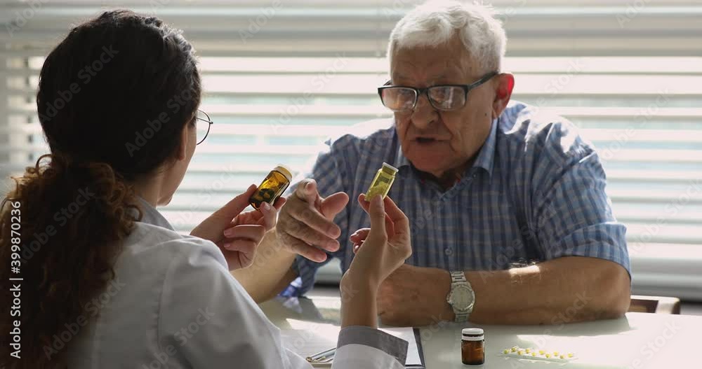 Female doctor talk to old unhealthy male patient during visit in private clinic, show bottles with meds explain prescription, give professional consultation. Chronic disease treatment pharmacy concept Female doctor talk to old unhealthy male patient during visit in private clinic, show bottles with meds explain prescription, give professional consultation. Chronic disease treatment pharmacy concept