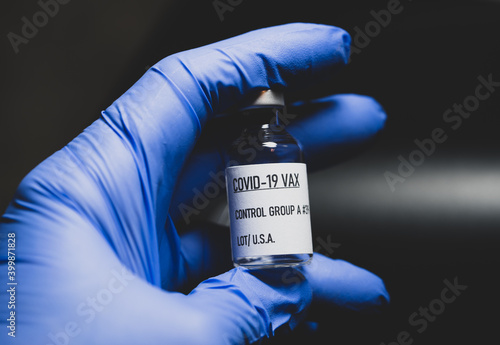 covid 19 vaccine bottle is being held by a hand with a blue latex glove