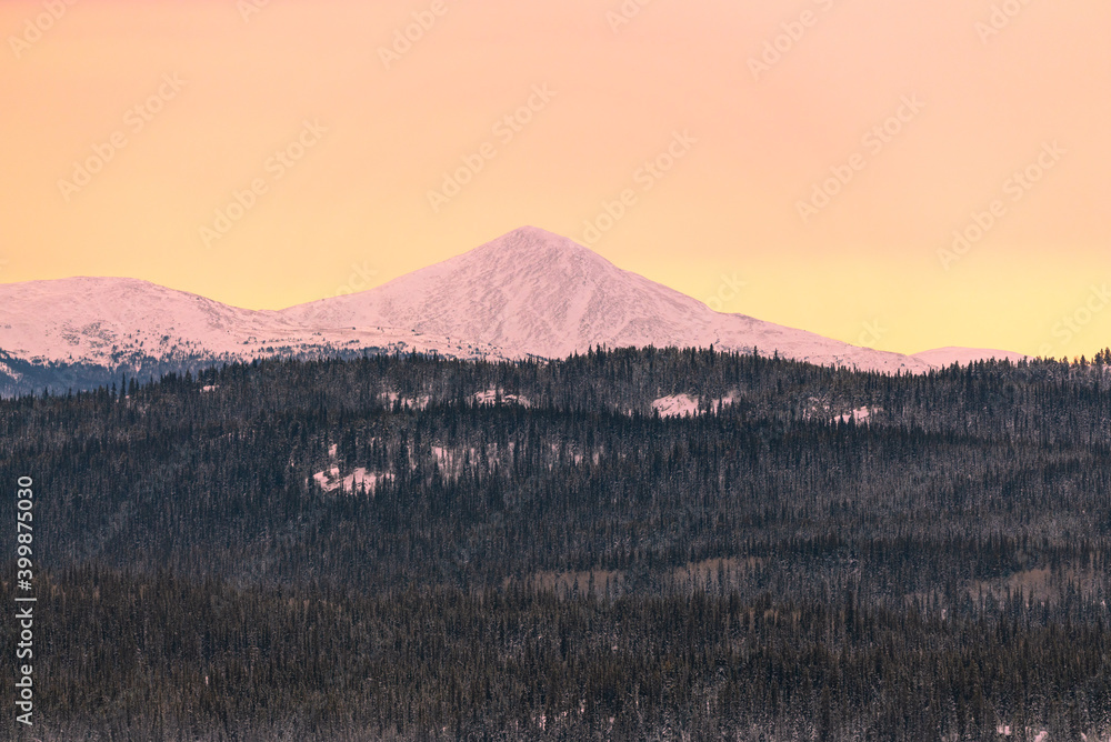 Beautiful pastel pink and orange sunset landscape view of snow capped mountains in northern Canada, Yukon Territory.  Stunning serene wilderness over frozen lake. 