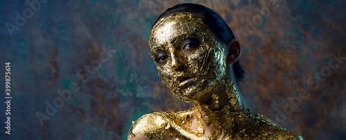 Girl with a mask on her face made of gold leaf. Gloomy studio portrait of a brunette on an abstract background.