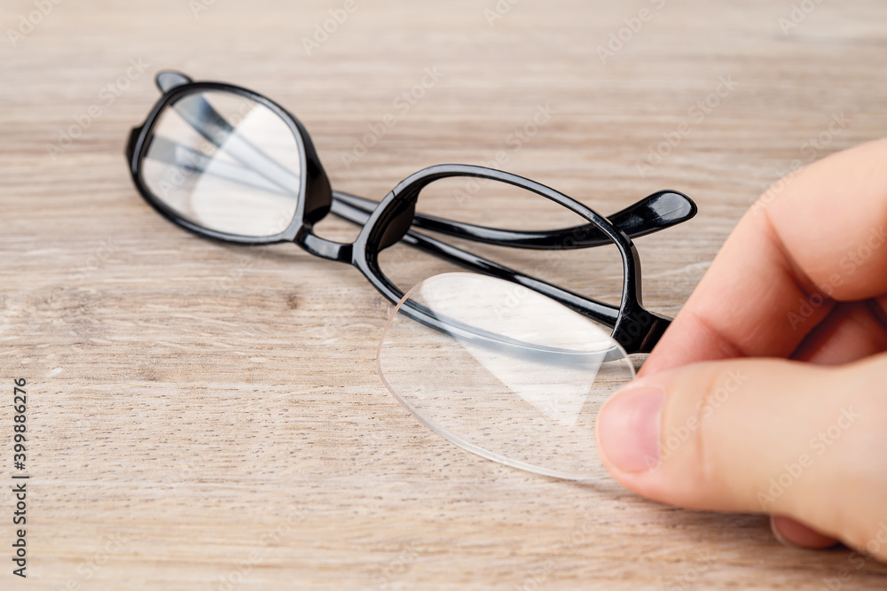 Fingers hold the fallen out lens in front of eyeglasses with the