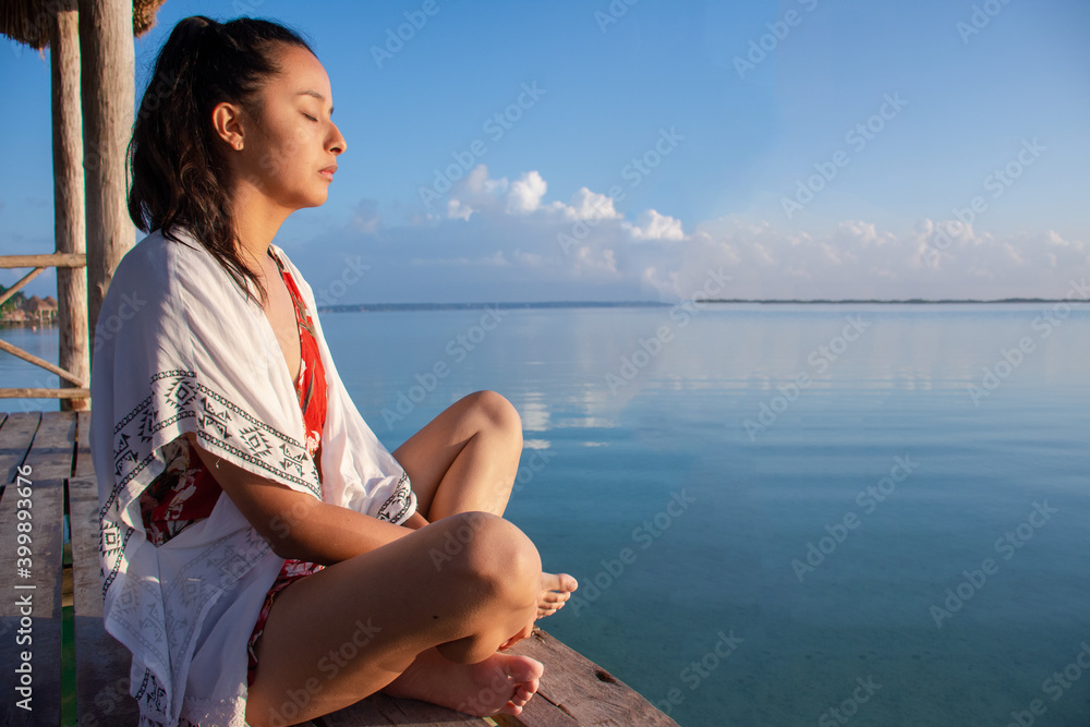 Young woman meditating on a dock in the sea
