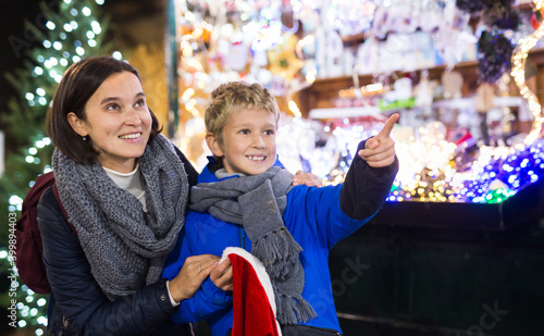 Cheerful tween boy looking for decorations on Christmas street market while shopping with his mother © JackF
