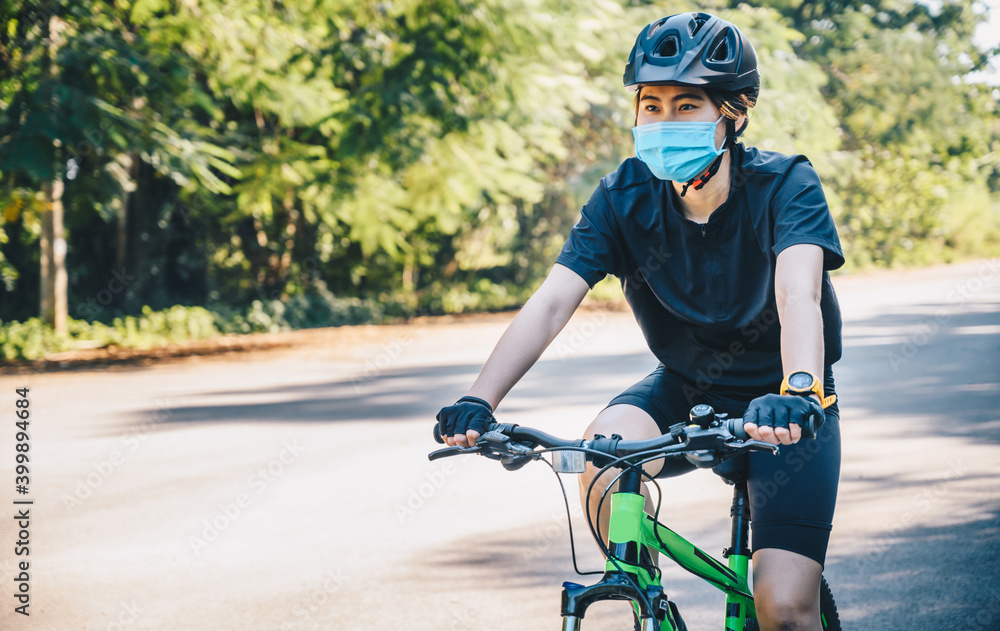 Young cyclist woman wearing a mask while riding a bicycle outdoor for protect and prevent the spread of virus. Conceptual of new normal lifestyle, everybody should wearing a mask when go outdoor. Young cyclist woman wearing a mask while riding a bicycle outdoor for protect and prevent the spread of virus. Conceptual of new normal lifestyle, everybody should wearing a mask when go outdoor.