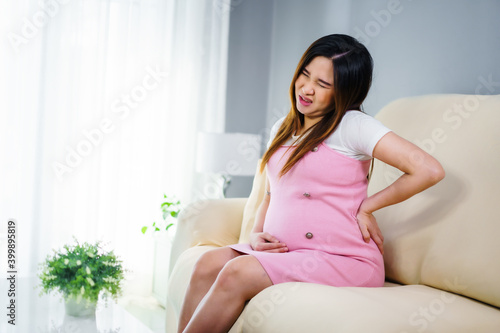 pregnant woman suffering lower back pain on sofa in living room