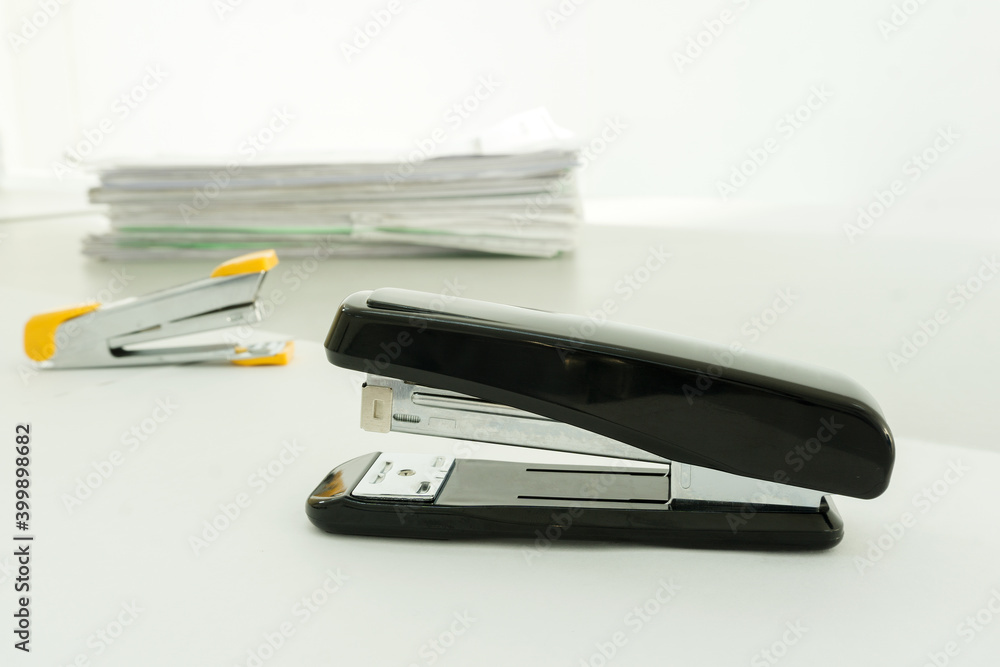 Black Stapler on desk office with blurred Pile of documents on background.