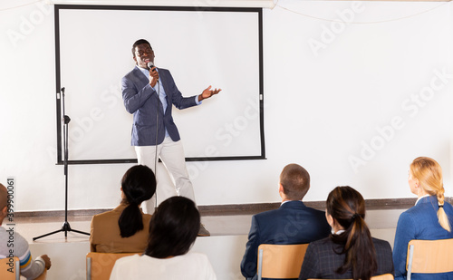 Young emotional male motivation coach giving speech from speaker stage