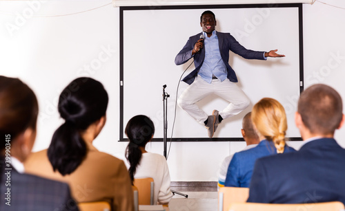 Expressive male lecturer speaking and jumping at corporate motivational coaching and training conference
