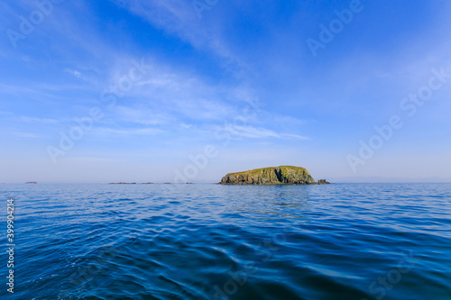 A small uninhabited green island in the middle of a calm blue sea and blue sky. Beautiful relaxation background.