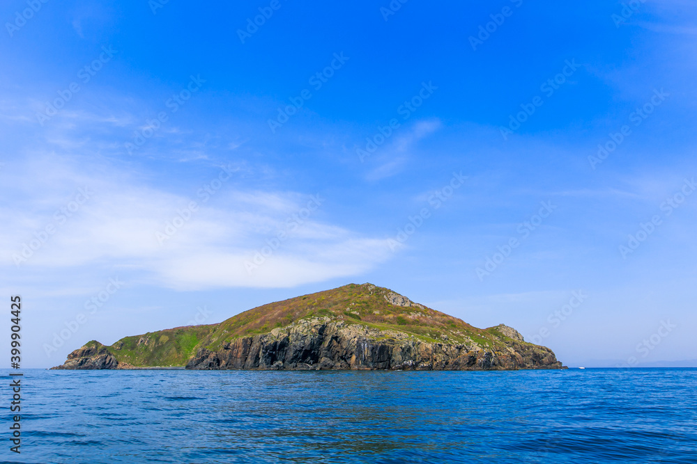 A small uninhabited green island in the middle of a calm blue sea and blue sky. Beautiful relaxation background.