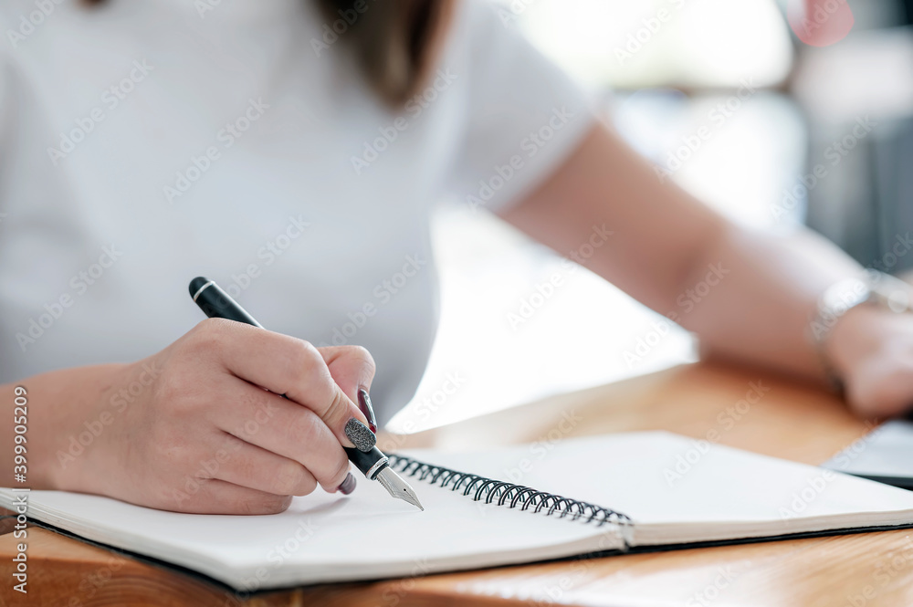 Closeup image of female hand writing on notebook with pen while sitting at the table. Closeup image of female hand writing on notebook with pen while sitting at the table.