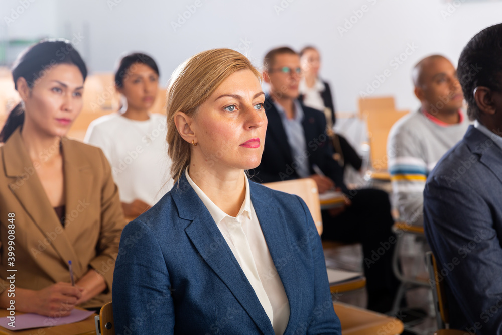 Fototapeta premium Portrait of focused female entrepreneur sitting with group of people in conference room during business event