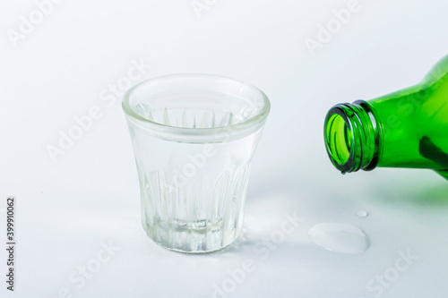Bottle and chilled shot glass of alcoholic beverage on white table. Rice vodka or wine