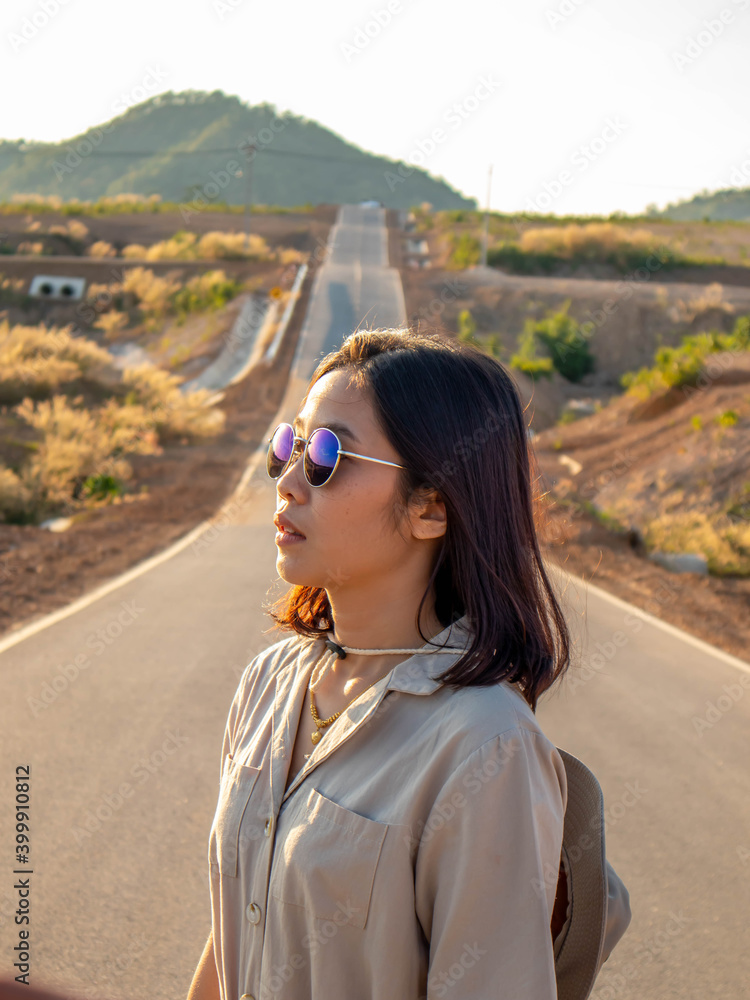 A woman wearing a hat and glasses is standing in the middle of the road. A woman wearing a hat and glasses is standing in the middle of the road.