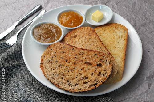 Whole grains bread with seeds served with kaya, butter and jam on a white plate.