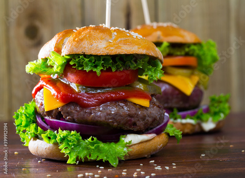 Two appetizing cheeseburgers with grilled beef patty, fresh vegetables and pickled cucumbers