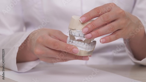 A woman orthodontist holds in her hand a plate for correcting teeth and occlusion. To put the plate on the plaster white teeth. Jaw treatment in a specialist doctor's office. A healthy and beautiful