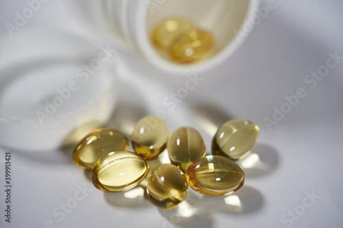 Omega-3 gel capsules with fish oil are poured from a bottle on a white background