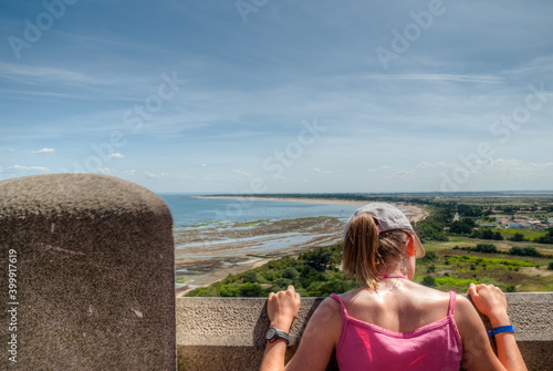 fille de dos casquette et t-shirt rose en haut d'un phare sur une ile de France en été photo