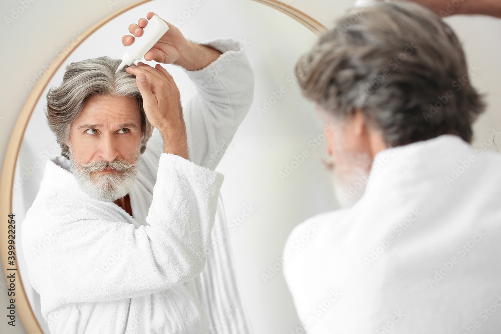Obraz premium Mature man using serum for hair loss treatment near mirror