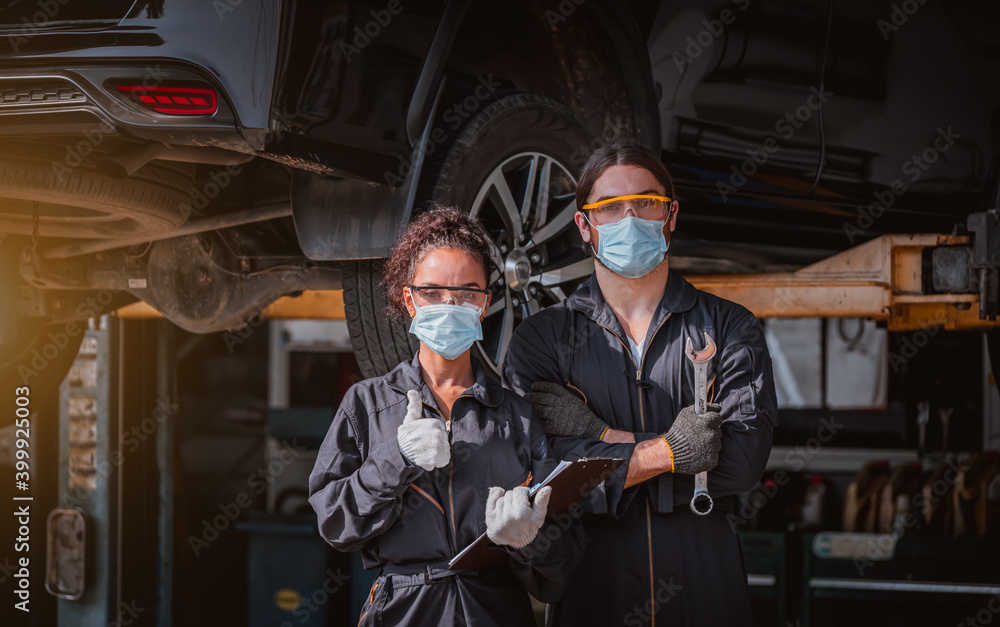 Portrait car mechenics posing under working at garage with showing screwdriver ,we wearing mask to protect virus and pollution.