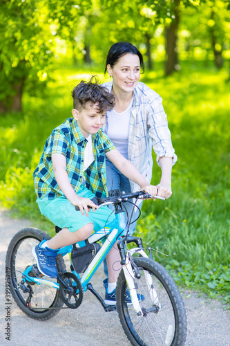 Mom helping her son learn to ride a bike in a summer park. Family weekend breaks.