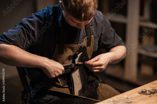 a young man is engaged in the family craft of making leather shoes in a workshop