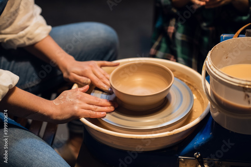 a young female potter teaches a small boy to make a pot of clay