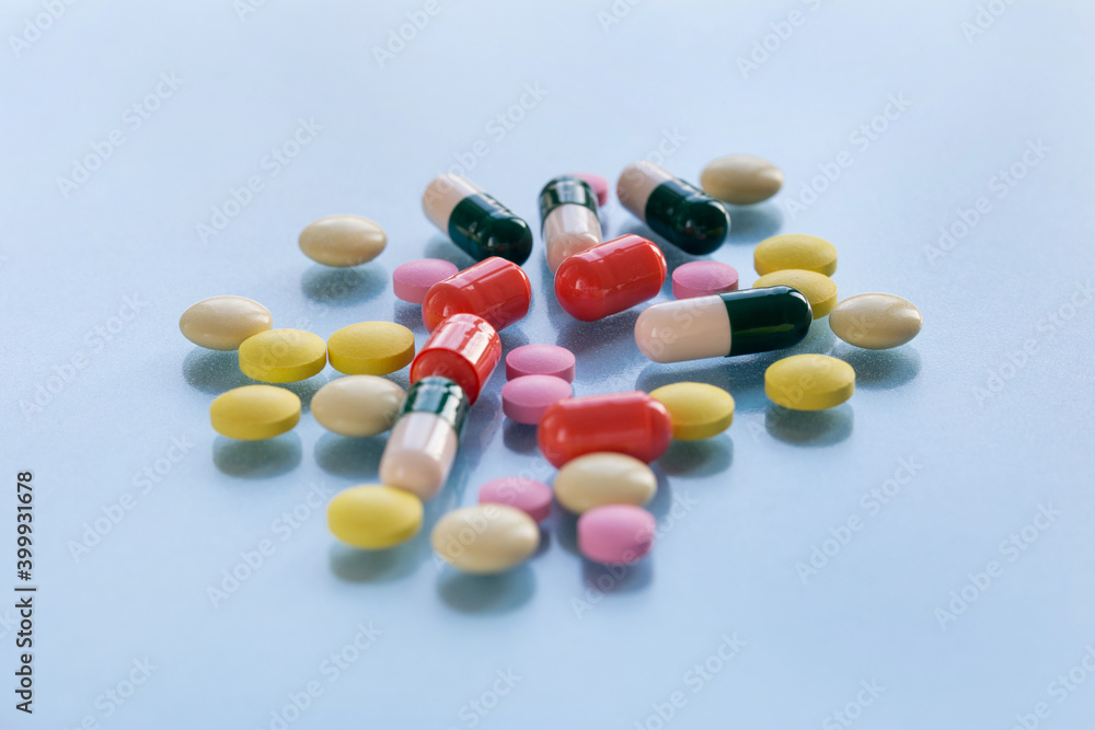 Colorful pills and capsules isolated on a blue background. Medical health or drugs addiction concept.