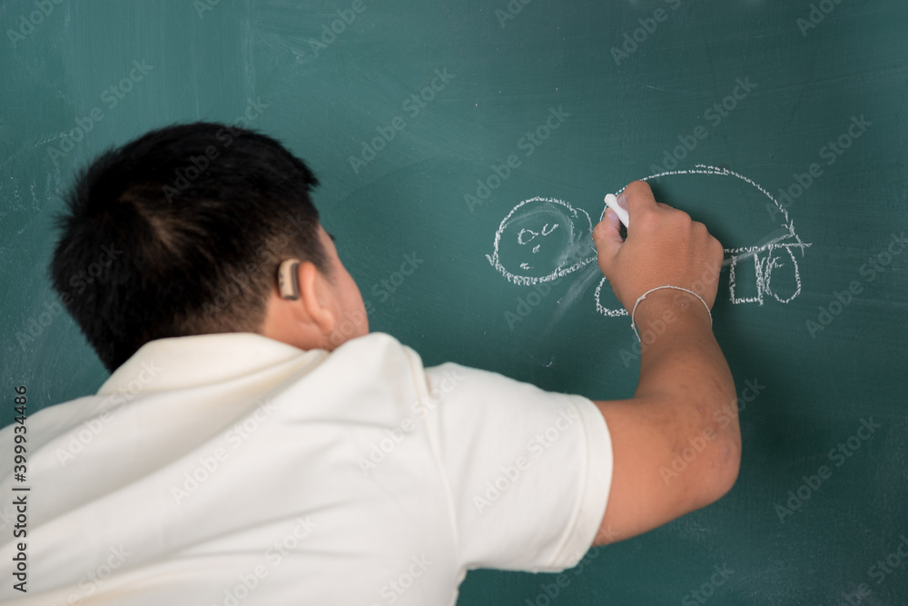 Asian disabled child boy wear hearing aid draw a picture on chalkboard