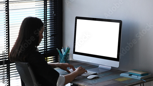 A young female designer sitting in front of her professional computer with blank screen at creative workplace.