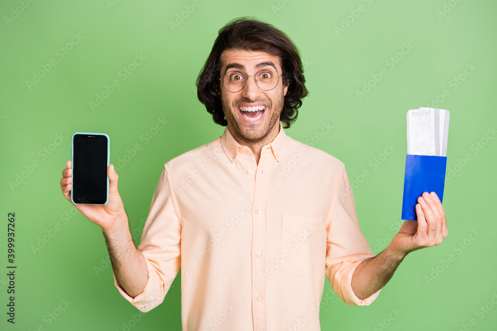 Portrait of attractive cheerful guy holding in hands gadget air ticket use app booking check-in isolated on bright green color background Portrait of attractive cheerful guy holding in hands gadget air ticket use app booking check-in isolated on bright green color background