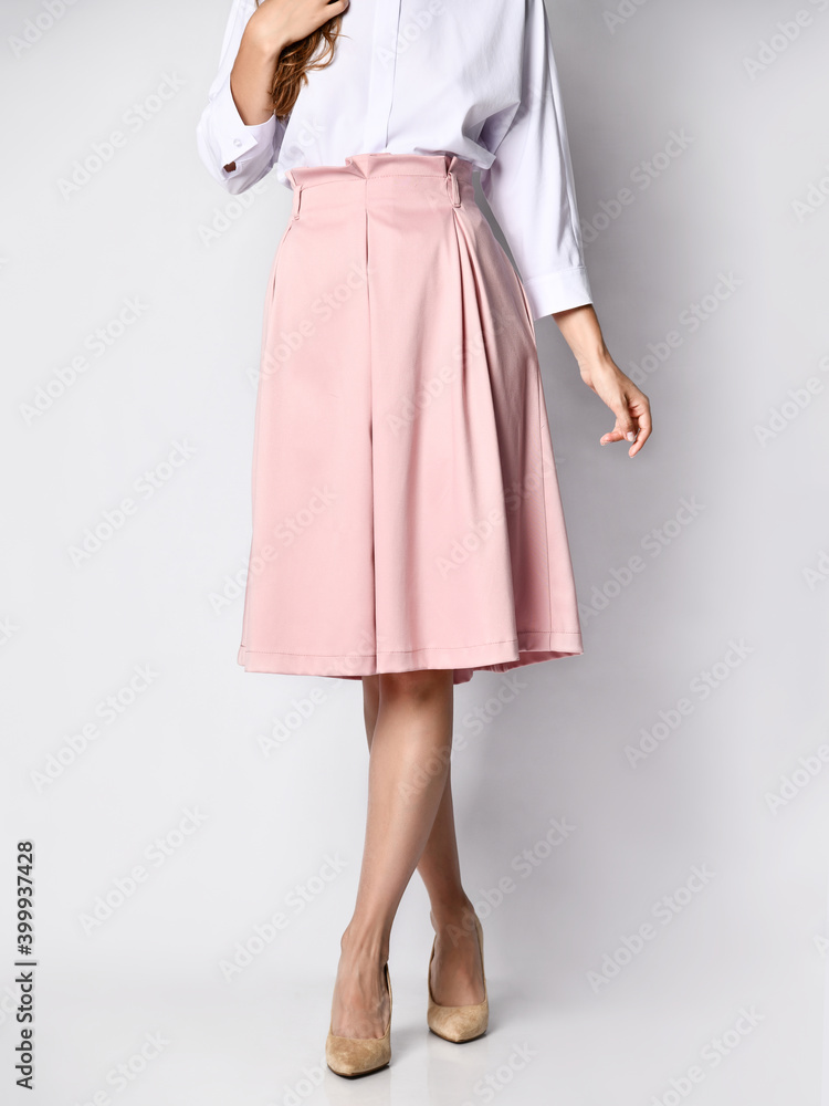 Cropped photo of young woman, posing in isolation, in an official light blouse, pink skirt and high-heeled shoes Cropped photo of young woman, posing in isolation, in an official light blouse, pink skirt and high-heeled shoes