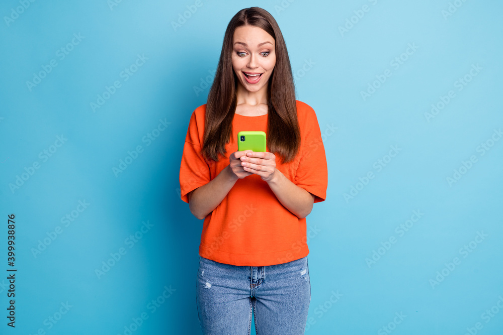Photo of surprised funny lady dressed denim pants orange t-shirt looking holding hands arms device isolated blue color background Photo of surprised funny lady dressed denim pants orange t-shirt looking holding hands arms device isolated blue color background