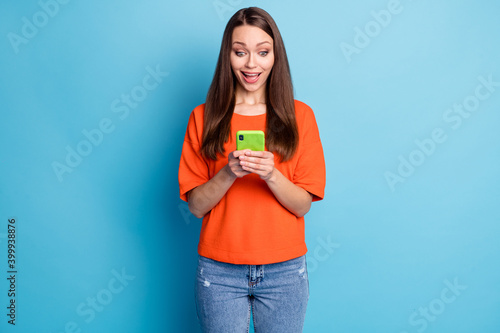 Photo of surprised funny lady dressed denim pants orange t-shirt looking holding hands arms device isolated blue color background