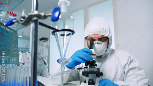 Medical research scientist conducting DNA experiments under microscope wearing protection suit in laboratory. Chemist examining virus evolution using high tech for vaccine development against covid19