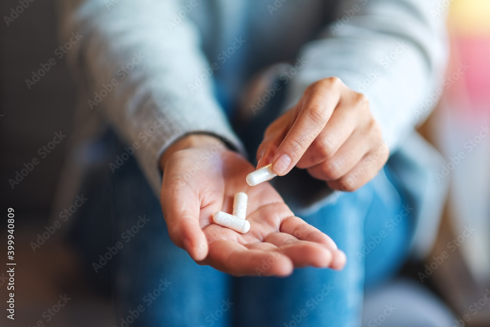 Closeup image of a woman holding and picking white medicine capsules in hand