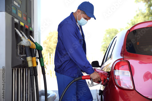 Worker in mask refueling car at modern gas station