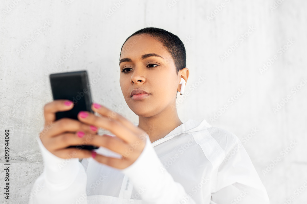fitness, sport and technology concept - young african american woman with wireless earphones listening to music on smartphone outdoors fitness, sport and technology concept - young african american woman with wireless earphones listening to music on smartphone outdoors