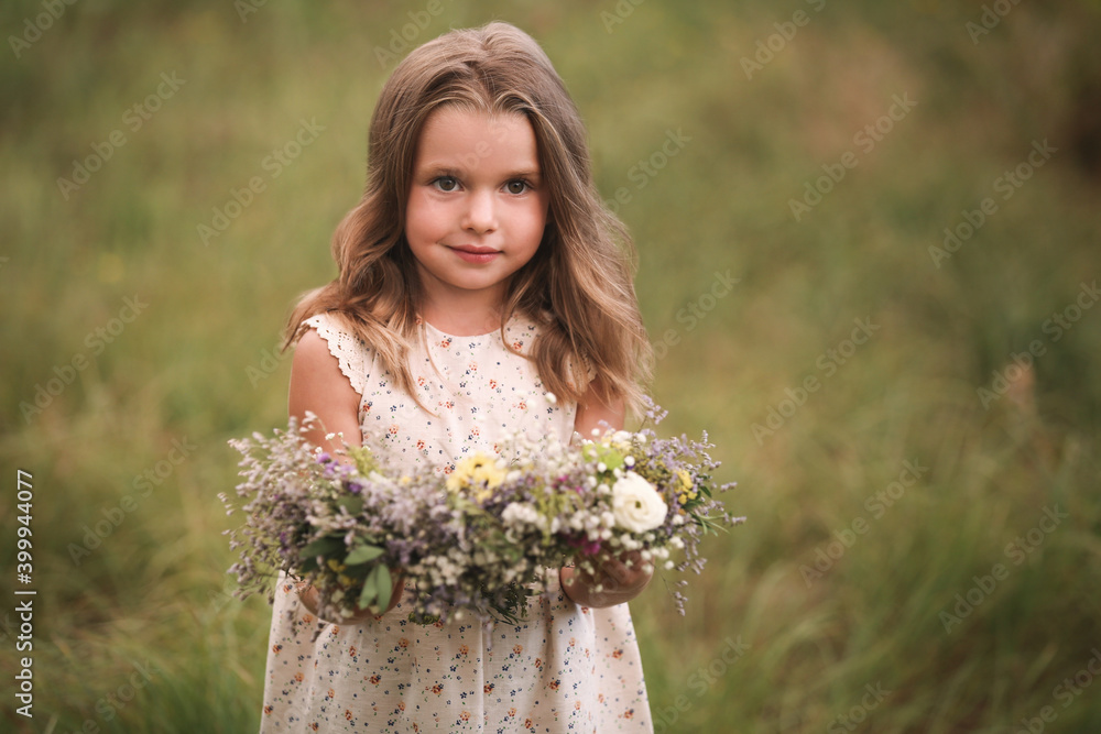 Naklejka premium Cute little girl holding wreath made of beautiful flowers in field