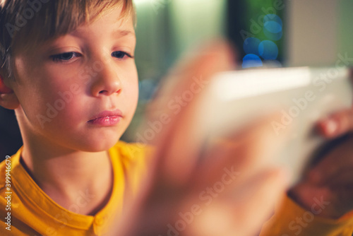 Close up face of a boy with smartphone playing a game, at home. Caucasian child spending time in a social network using mobile phone. White kid using cell phone for gaming. People and social media