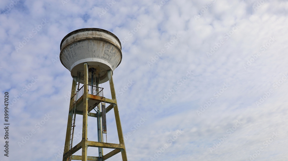 Concrete water tank on a tall tower. Large outdoor white water reserve tank for urban water supply system On the sky background there are white clouds with a copy space. Selective focus
