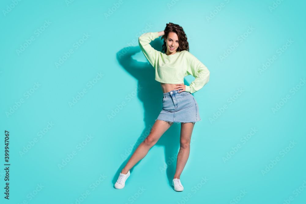 Full length body size photo of cheerful fit girl wearing casual clothes touching hair isolated on vibrant teal color background Full length body size photo of cheerful fit girl wearing casual clothes touching hair isolated on vibrant teal color background