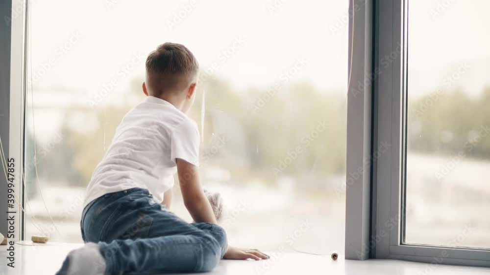 Boy sits on the windowsill and looks out the window. Boy sits on the windowsill and looks out the window.