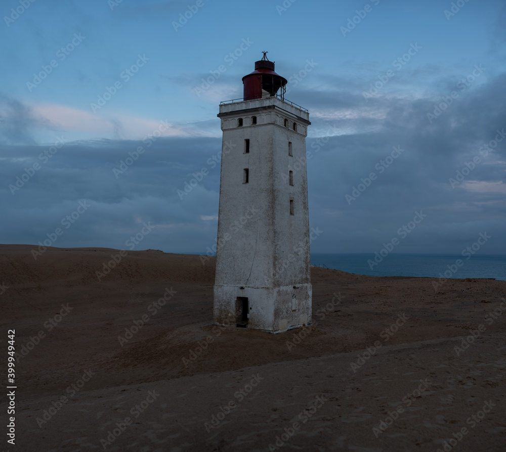 The lighthouse stands on the sand against the background of clouds and the sea in the early morning in cloudy weather