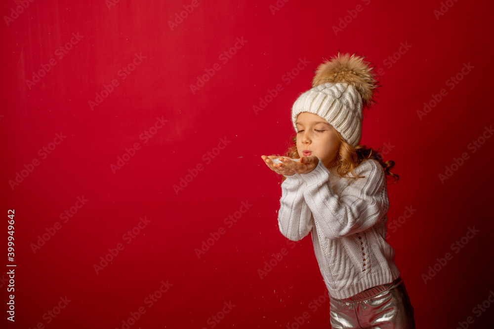 girl in hat blowing on snow on red background girl in hat blowing on snow on red background