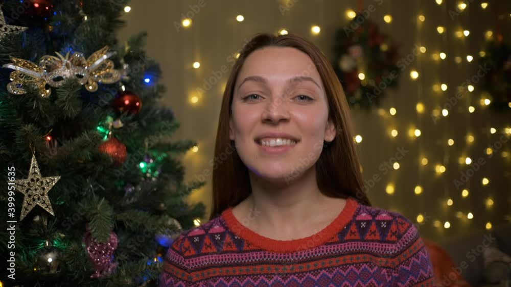 Smiling woman wishing a merry Christmas, Christmas tree and decorated room interior in the background Smiling woman wishing a merry Christmas, Christmas tree and decorated room interior in the background