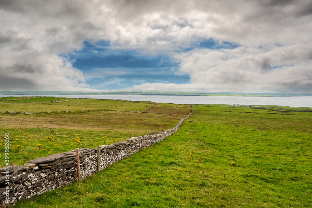Traditional dry stone fence in a field with green grass. West coast of Ireland. Nobody. Beautiful cloudy sky. Rural area